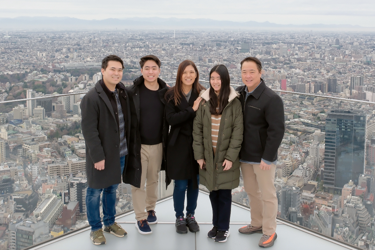 The Hisanaga family pose for a photo on top of a skyscraper with a cityscape behind them.