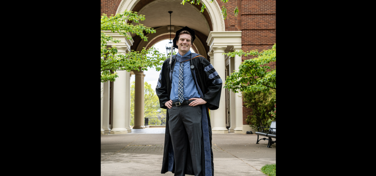 Dr. Patrick Callagy in full doctoral regalia stands in front of archway of Weatherford Hall.