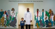 Dr. Masson Blow and son Maddix pose in the middle of the mural gifted to the college by the class of 2021.