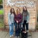 Three women and one black lab dog in front of sign that says Guide Dogs for the Blind